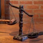Photo of a scale with a revolver in one pan and the hammer of justice in the other pan.