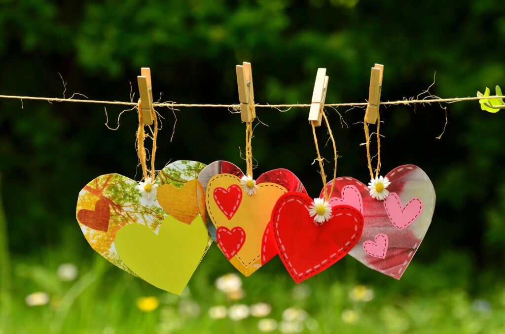 Multicolored hearts hung on a clothesline with clothespins.